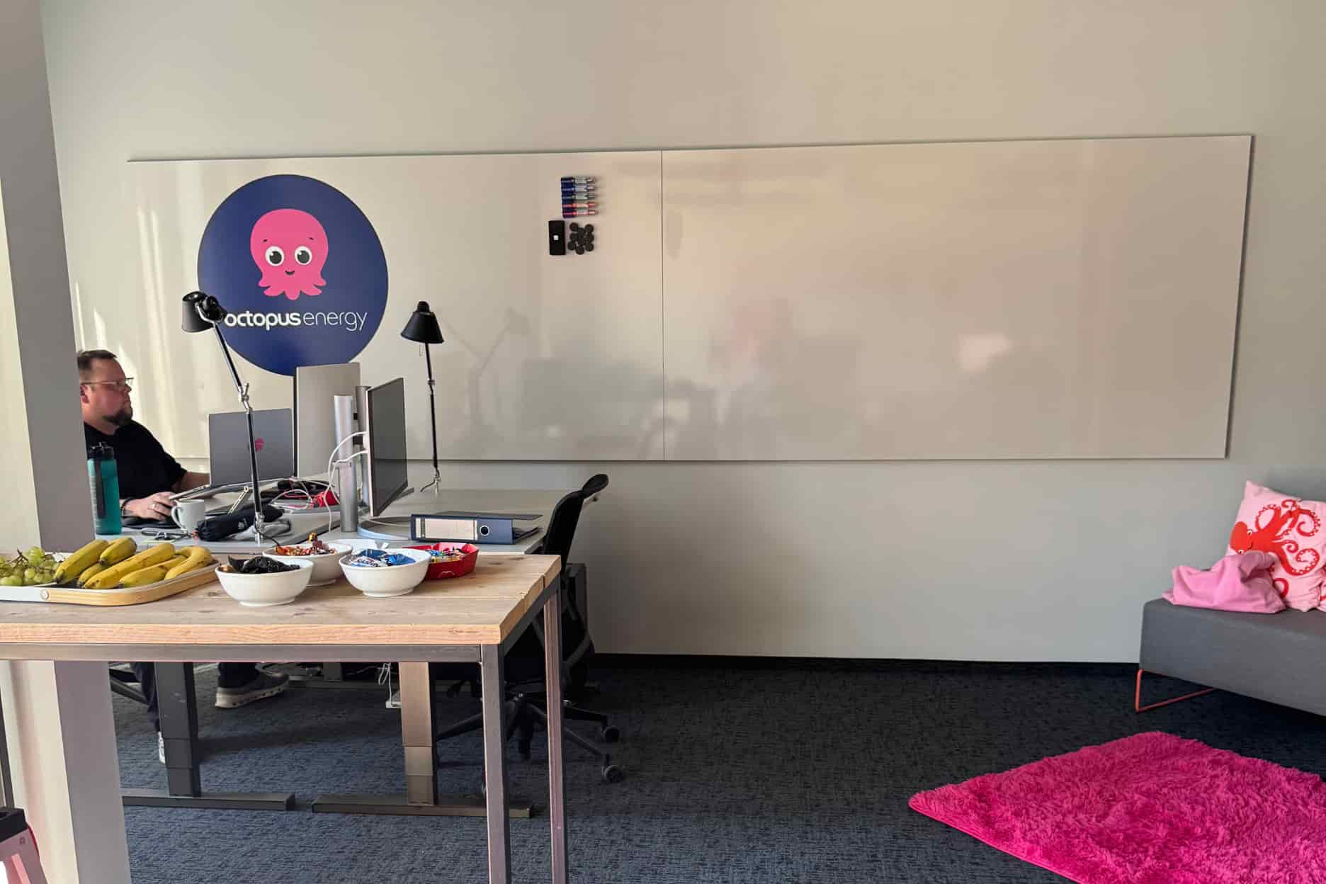 Ein Whiteboard mit Octopus Energy Logo. Im Vordergrund sind Schalen mit Snacks un Obst zu sehen.